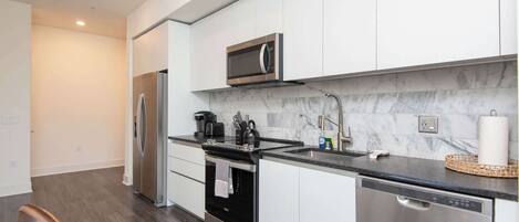 Una cocina moderna con electrodomésticos de acero inoxidable, un salpicadero de mármol y encimera negra.