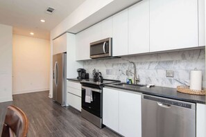 A modern kitchen with stainless steel appliances, a marble backsplash, and a black countertop.