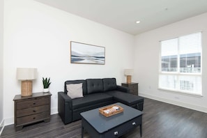 A modern living room with a black sofa, a coffee table, and a painting on the wall. - Hollywood 2BR apt w Rooftop deck & Stunning Views (Los Angeles)