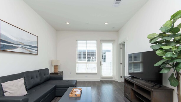 A modern living room with a black sectional sofa, a coffee table, a flat-screen TV, and a large green plant.