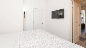 A bedroom with a bed, a wall-mounted TV, a door, and a floor lamp.