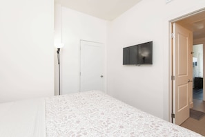 A bedroom with a bed, a wall-mounted TV, a door, and a floor lamp.