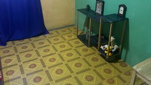 Une pièce avec un sol à motifs, un rideau bleu, une petite table avec une horloge et une étagère remplie de peluches.