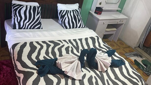 Un lit bien fait, avec une literie et des oreillers à motifs zébrés, une tête de lit en bois et une petite table de chevet agrémentée d’un miroir et de produits de toilette.