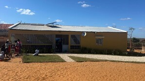 Un bâtiment doté d’un toit en tôle ondulée et d’une façade plate, entouré d’une zone sablonneuse où l’on peut voir des empreintes de pas.