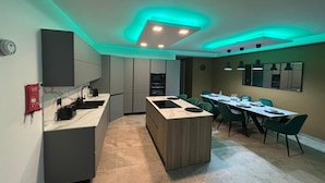 Une cuisine moderne dotée d’un îlot central, d’un coin repas avec des chaises vertes et d’un éclairage au plafond de couleur turquoise.