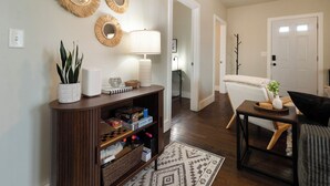 A living room with a sofa, a coffee table, and a side table. There is a bookshelf with various items on it, and a door leading to another room. - Stylish Groton Getaway • Updated 2BR close to Navy Base-Casinos-Mystic & Beaches (Groton)