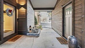Un paseo techado que conduce a una casa con garaje, un lazo en la puerta y un pequeño jardín con rocas y plantas.