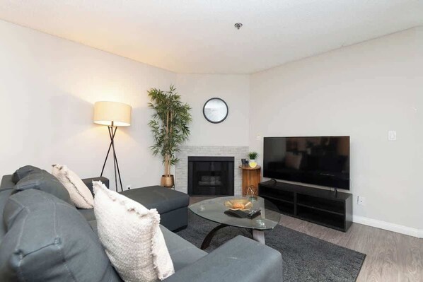 A living room with a sofa, a coffee table, a lamp, a television, and a fireplace. - Stylish Hollywood 2BR apt with Rooftop Pool (Los Angeles)
