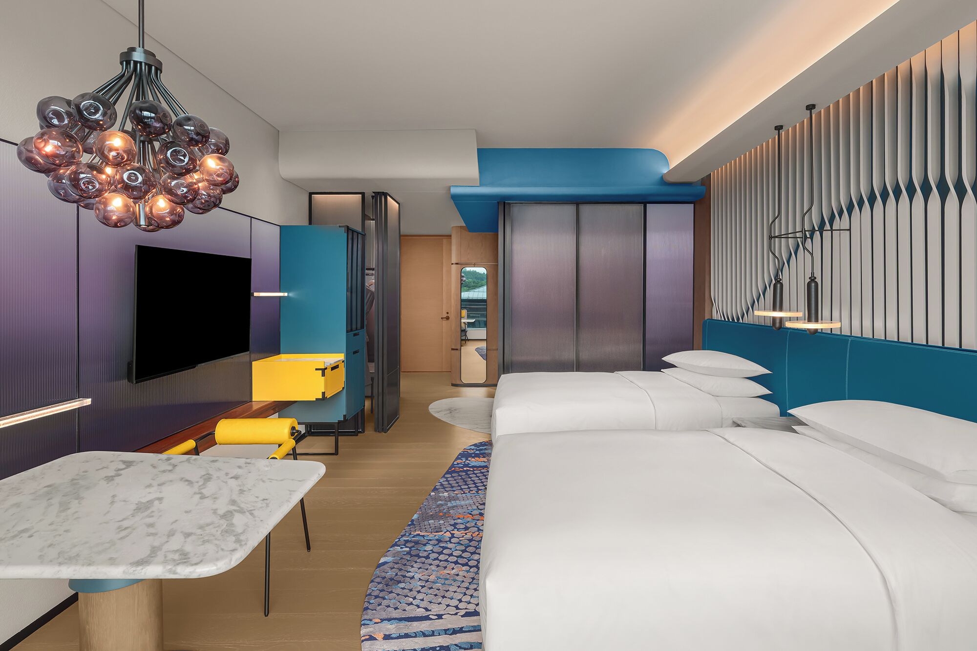 A modern hotel room with a large bed, a TV, a dining area, and a unique wall design.