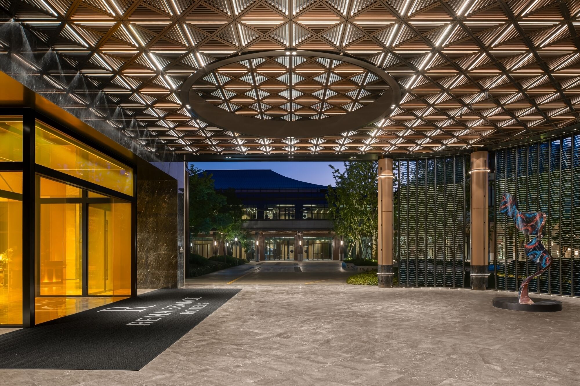 En moderne hotelindgang med et geometrisk loftsdesign, et receptionsområde og en skulptur.
