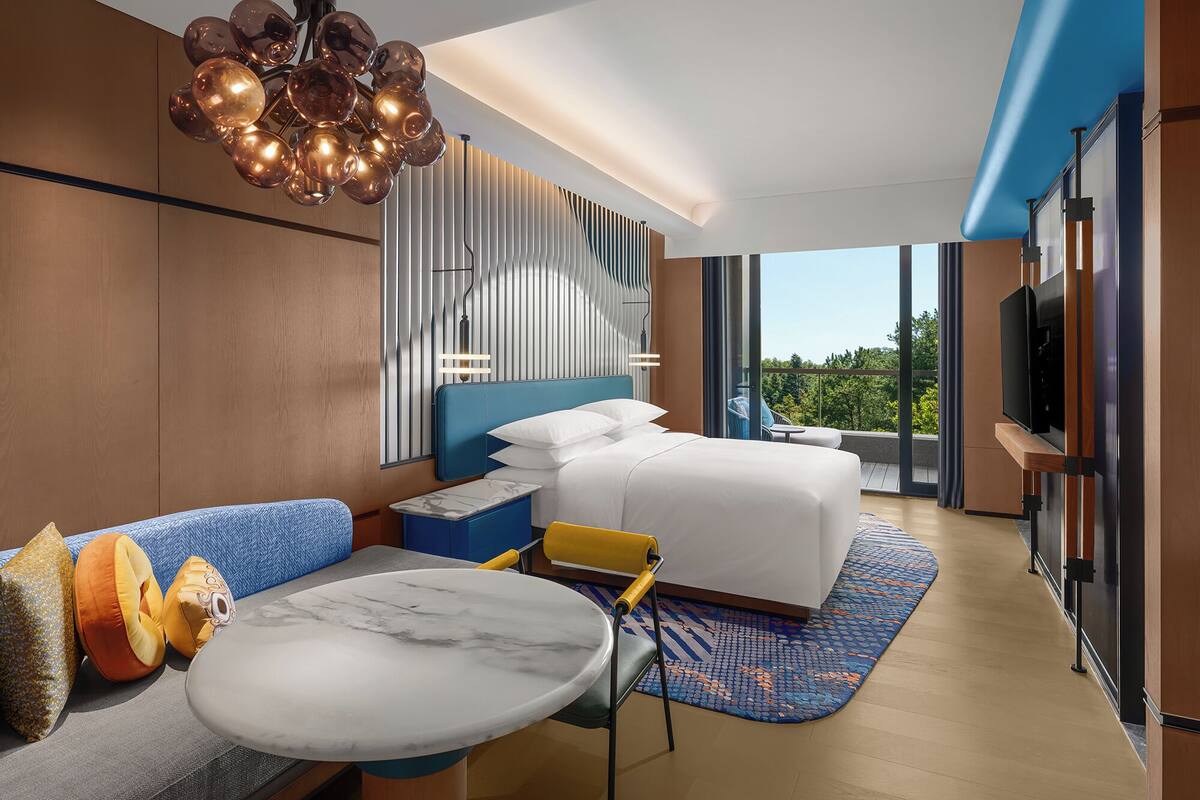 Habitació d'hotel moderna amb un llit gran, un sofà, una taula de menjador i un balcó amb vistes.
