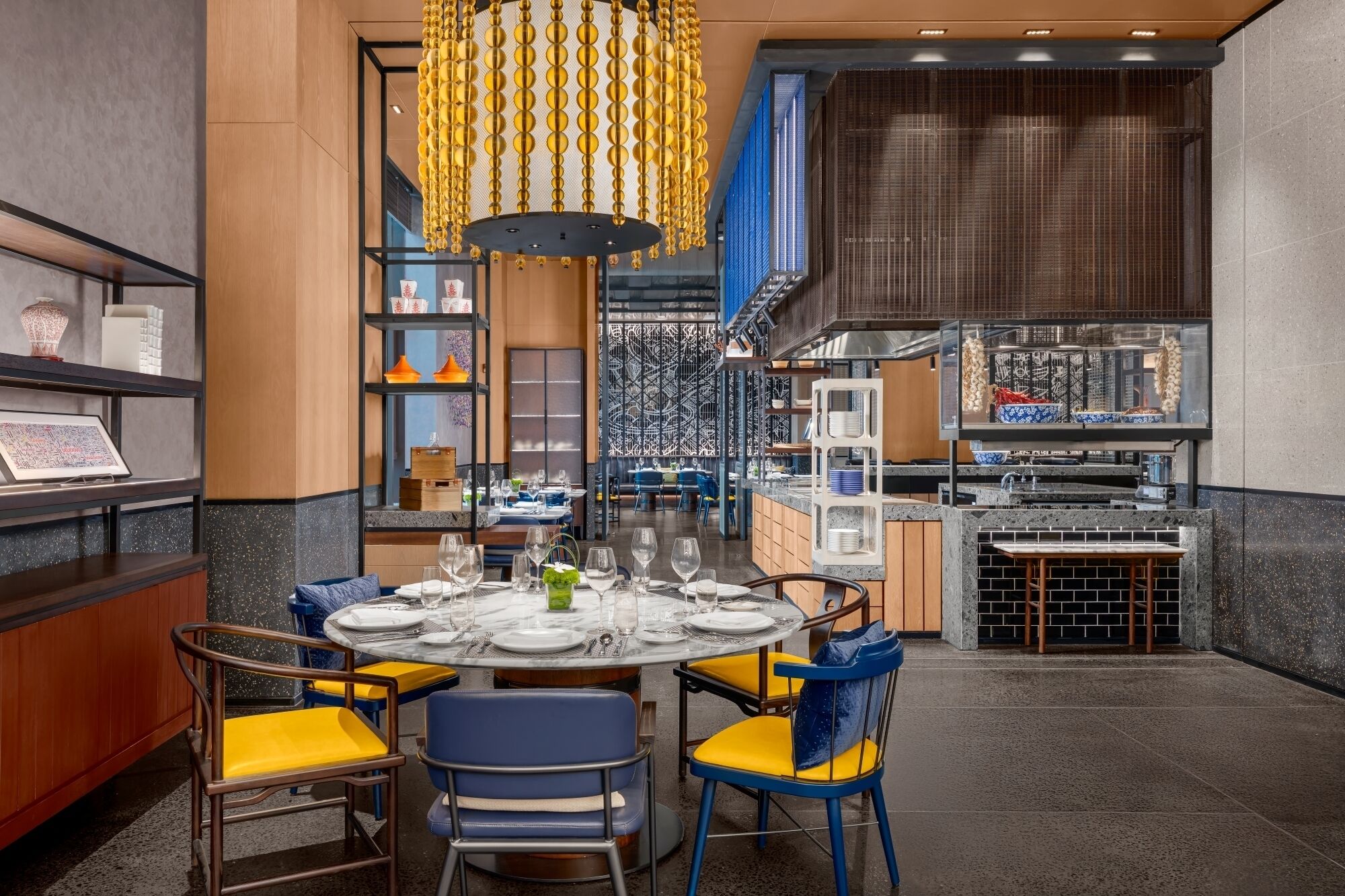 A restaurant interior with a round dining table, blue and yellow chairs, and a hanging golden ornament.