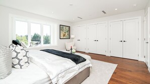 A modern bedroom with a large bed, white walls, and a view of greenery outside. - 3 bed 3.5 bath modern luxurious home. Minutes to downtown, Airport and Granville (Vancouver)
