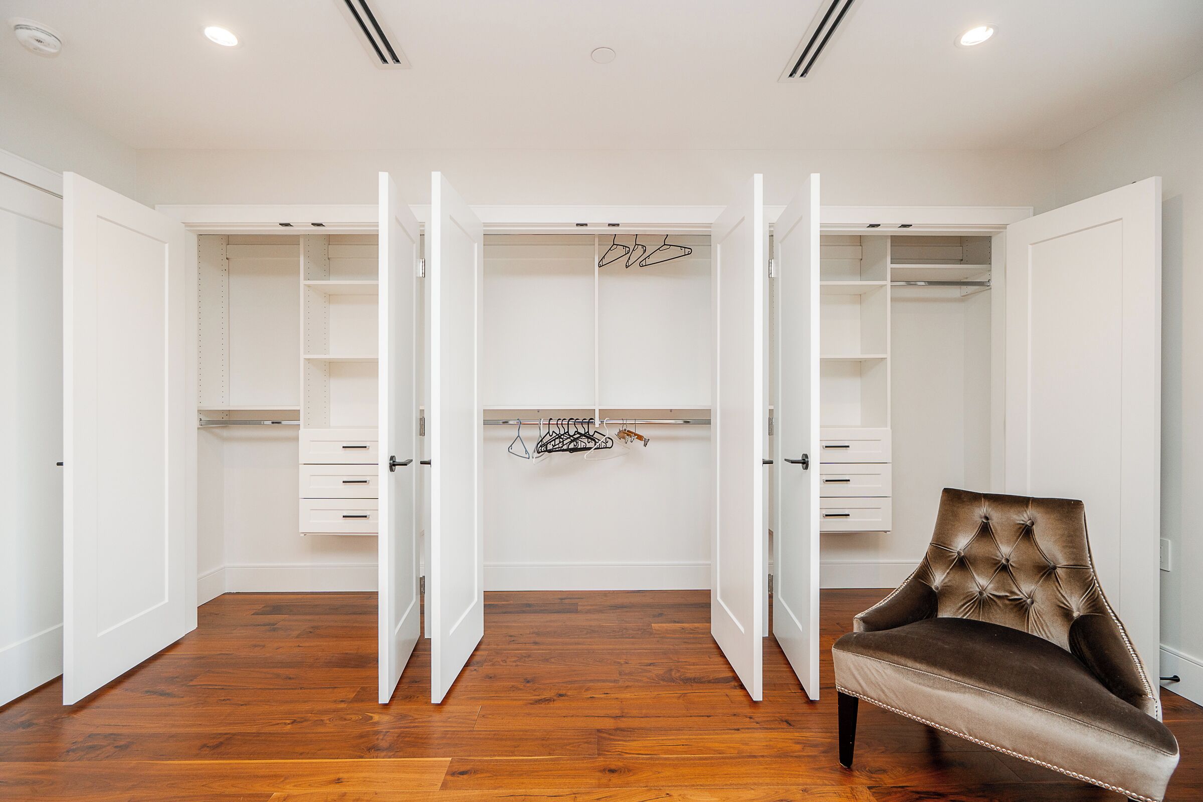A walk-in closet with open doors, a hanging rod, and a velvet chair.