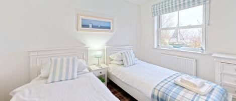 Een tweepersoonskamer met twee bedden, een nachtkastje met een lamp, een raam met uitzicht en een ingelijst schilderij aan de muur.