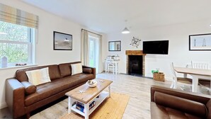 Ein modernes Wohnzimmer mit einem braunen Ledersofa, einem Holztisch und einem Essbereich mit weißem Tisch und Stühlen.