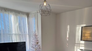 A modern living room with a flat-screen TV, a white Christmas tree, a blue sofa, and a glass coffee table. - Coastal comforts (Portsmouth)