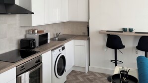 A compact kitchen with white cabinets, a built-in oven, a microwave, a washing machine, and a toaster. - Coastal comforts (Portsmouth)