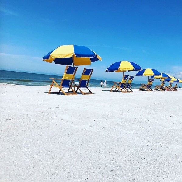 Una playa con hileras de sillas y sombrillas azules y amarillas.