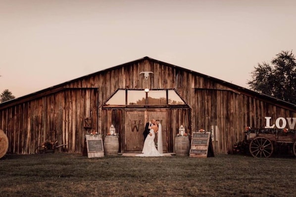 A rustic barn with a large wooden door, a sign with the word 'LOVE', and a vintage wagon.
