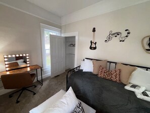 A bedroom with a bed, a vanity with lights, a guitar, and a door leading to a balcony.