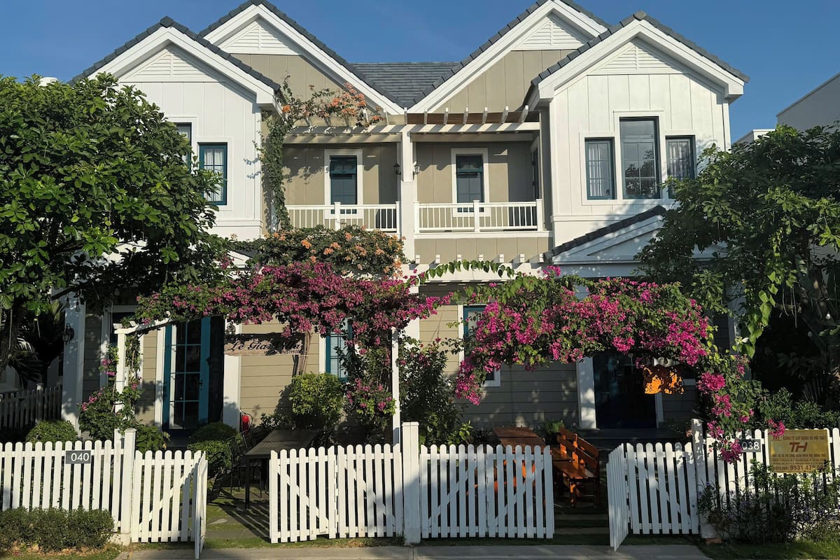 A two-story building with a white picket fence, a balcony, and flowering plants.