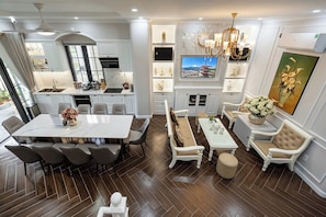 A modern kitchen with a dining area, a living room with a sofa and a TV, and a decorative wall with a painting. - Le Gia Villa Nova World Phan Thiet (Tien Thanh)