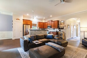 A spacious living room with a sectional sofa, a dining area with wooden cabinets, and a kitchen with stainless steel appliances.