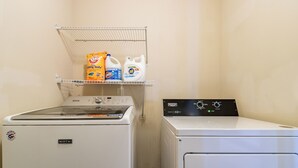 A laundry area with a front-loading washer and dryer, a shelf with detergent and fabric softener, and a metal rack.