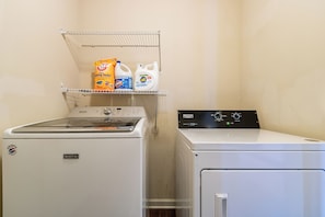 A laundry area with a front-loading washer and dryer, a shelf with detergent and fabric softener, and a metal rack. - Peaceful 2-bedroom house with office in charming Dallas (Dallas)