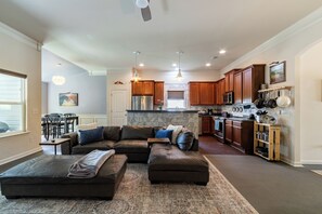 A spacious living room with a sectional sofa, ottoman, and a dining area with chairs.