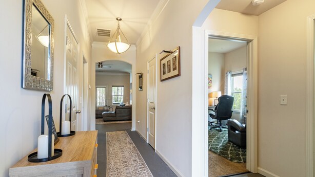 A hallway with a wooden console table, a patterned rug, and a door leading to a living area with a sofa and a chair.