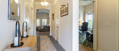 Un couloir avec une console en bois, un tapis à motifs et une porte donnant sur un espace de vie comprenant un canapé et un fauteuil.
