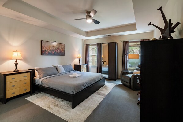 A bedroom with a bed, nightstands, a ceiling fan, a painting, and a view through a window.