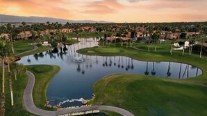 Un parcours de golf avec un étang, des palmiers et un coucher de soleil.