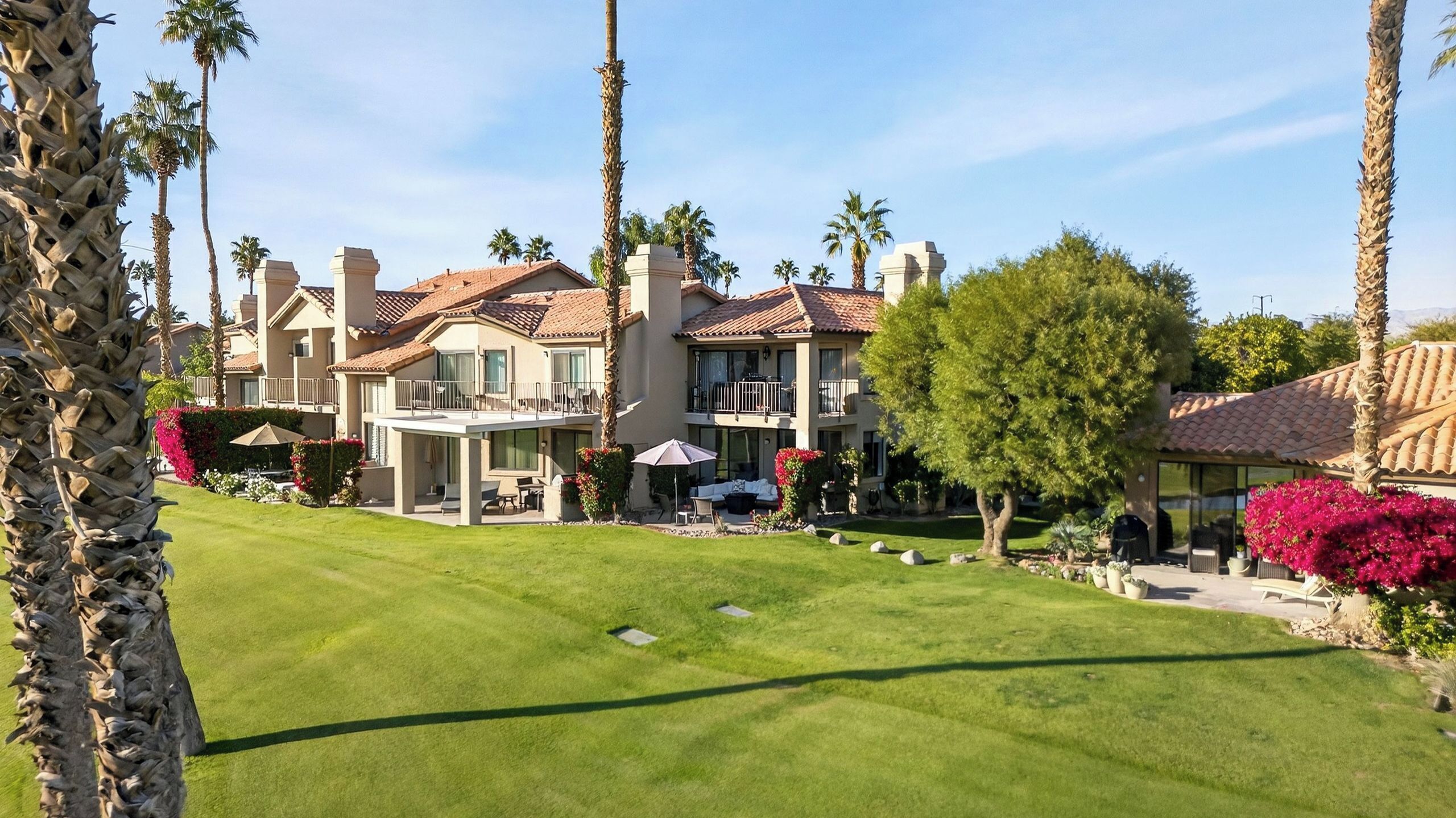 A residential building with a well-maintained lawn, multiple balconies, and surrounding palm trees.