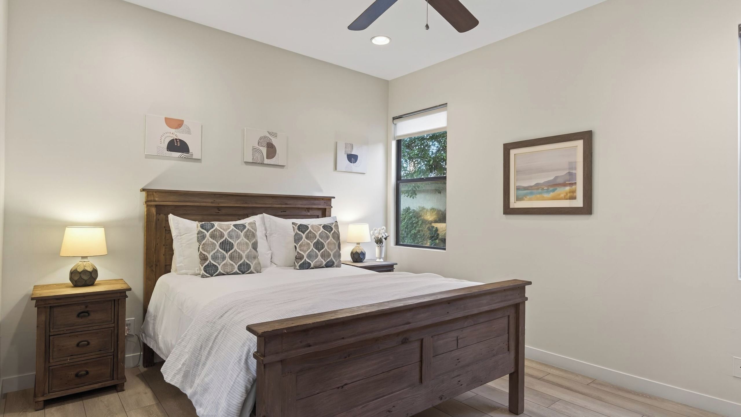 A bedroom with a wooden bed, bedside tables, a ceiling fan, and artwork on the walls.