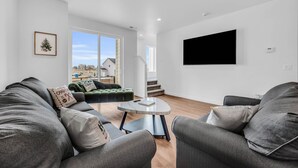 A modern living room with a grey sofa, a green armchair, a round coffee table, and a large TV mounted on the wall. - Wasatch Mountain Retreat. Your Ultimate Mountain Gateway in Mountain Green, Utah (Mountain Green)