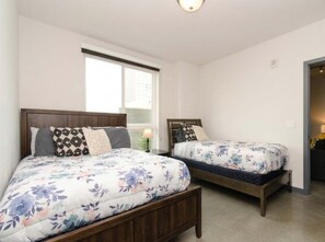 A bedroom with two beds, a window, and a door. - Chic Urban 2BR Getaway with Rooftop Pool Access (Los Angeles)