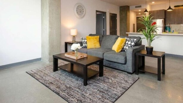 Ein modernes Wohnzimmer mit einer Couch, einem Couchtisch und Beistelltischen. Im Hintergrund befindet sich eine Küchenzeile.