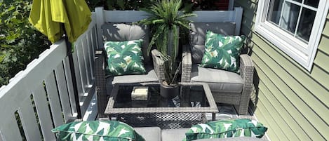 A sunlit outdoor seating area with wicker furniture, a small table, and a potted plant.