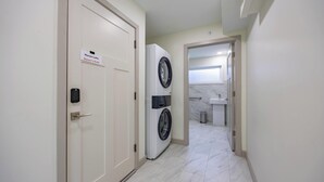 A hallway with a washing machine, a door labeled "Monon Lofts Owner's Suite," and a bathroom with a sink and mirror. - Monon Trail Lofts Luxury Studio With Hot Tub (Indianapolis)