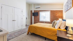 A bedroom with a bed, a TV mounted on the wall, and a window with blinds. - Monon Trail Lofts Luxury Studio With Hot Tub (Indianapolis)