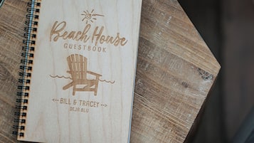 A wooden guestbook titled "Beach House Guestbook" with a sun and chair icon, and names "Bill & Tracey" and "Deja Blu" written on it.