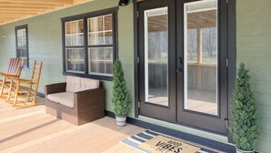 Un porche cubierto con un sofá de mimbre, sillas de madera mecedoras y una puerta con la inscripción 'Cove Sweet Cove'.