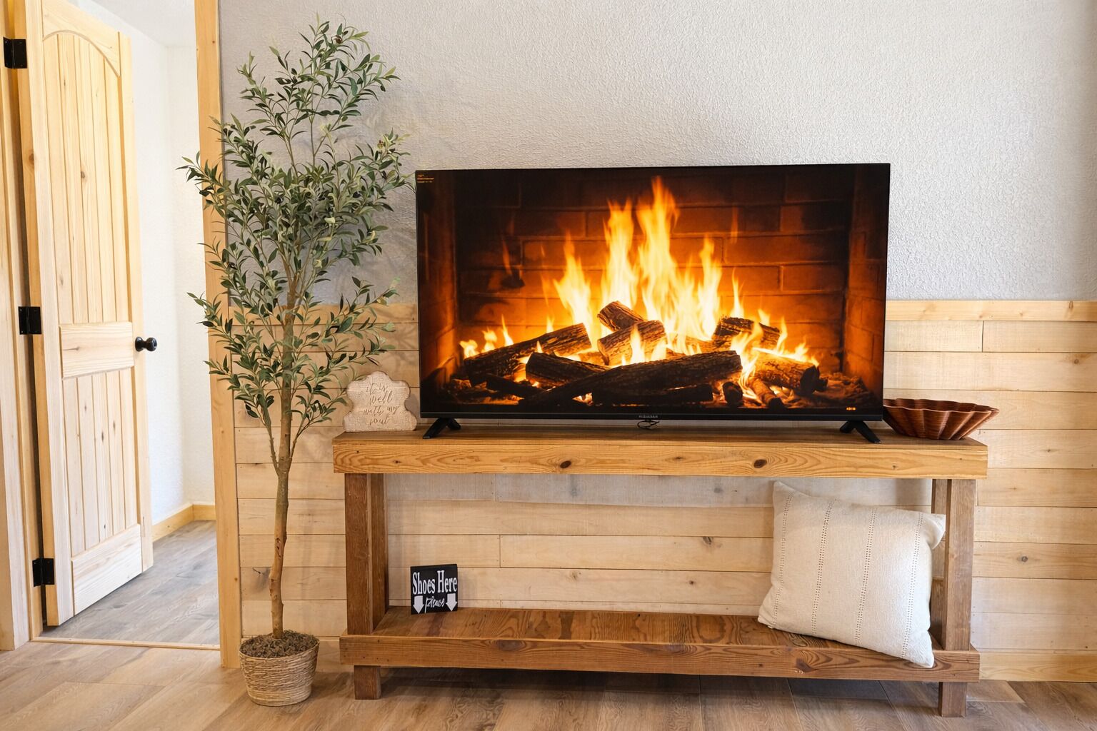 A fireplace with a TV above it, a wooden bench below, and a plant to the left.