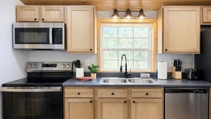 Una cocina moderna con armarios de madera, electrodomésticos de acero inoxidable, un ventanal con luz natural y un lavamanos con grifo.