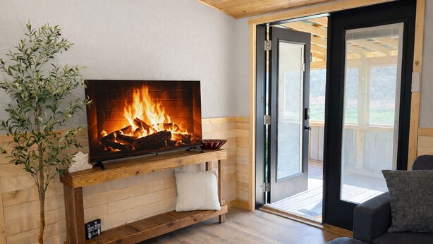 Una sala de estar acogedora con chimenea, suelo de madera, un sofá y una puerta corrediza de vidrio que da a un espacio exterior.