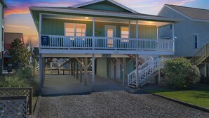 Une maison de plage à deux étages, dotée d’un balcon, d’une véranda et d’un escalier menant à l’étage supérieur.